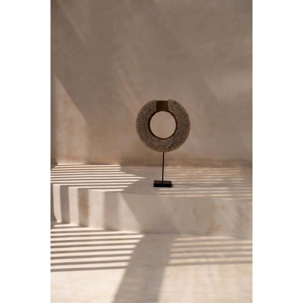 Sculpture circulaire sur socle, ombre rayée.